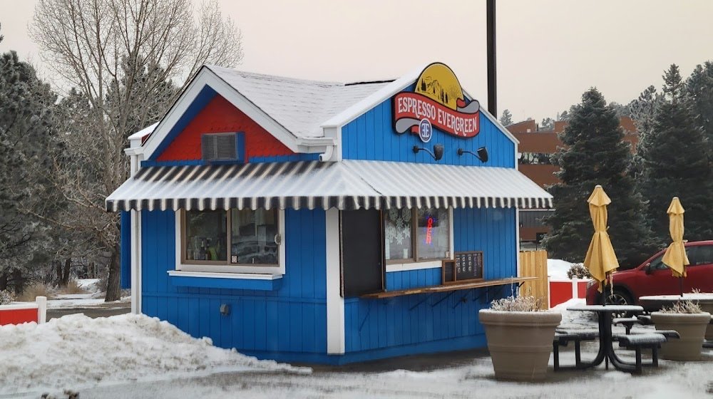 Espresso Evergreen after the rebrand: a bright blue hut with white trim, a red gable, a striped awning, a new illuminated sign and outdoor seating.